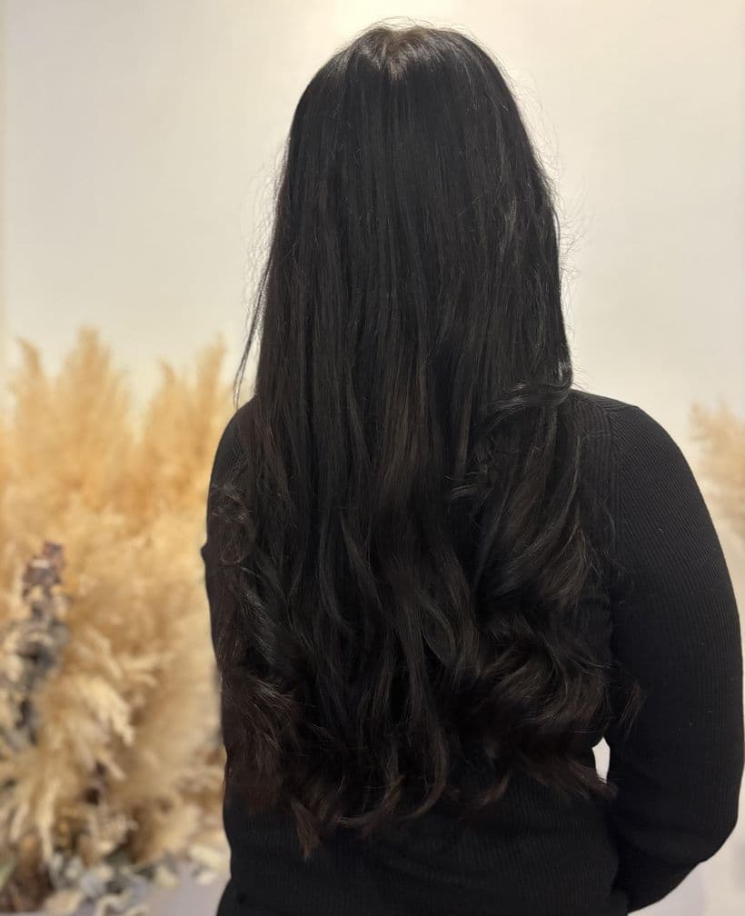Haarverlängerung und Haarverdichtung, nachher: Dunkles Haar, vorher flach anliegend und dünn auslaufend. Danach deutlich mehr Länge und Volumen, in Wellen gestylt.
